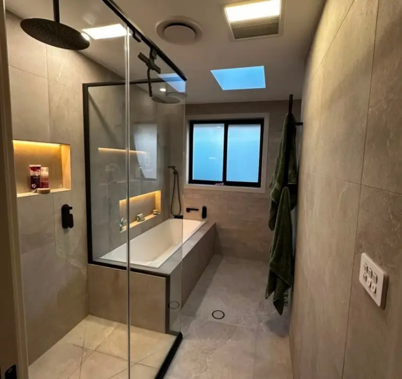 Complete modern bathroom renovation in Belconnen featuring marble-look wall tiles, timber vanity, and black tapware.